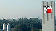 Baumit logo on a tall grey building in front of trees with a city in the background