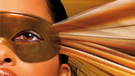 A womans eye behind a gold mask with golden fabric 